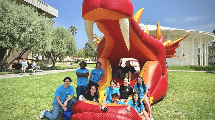 Group of students in blue shirts sitting in inflatable red dragon bounce house.